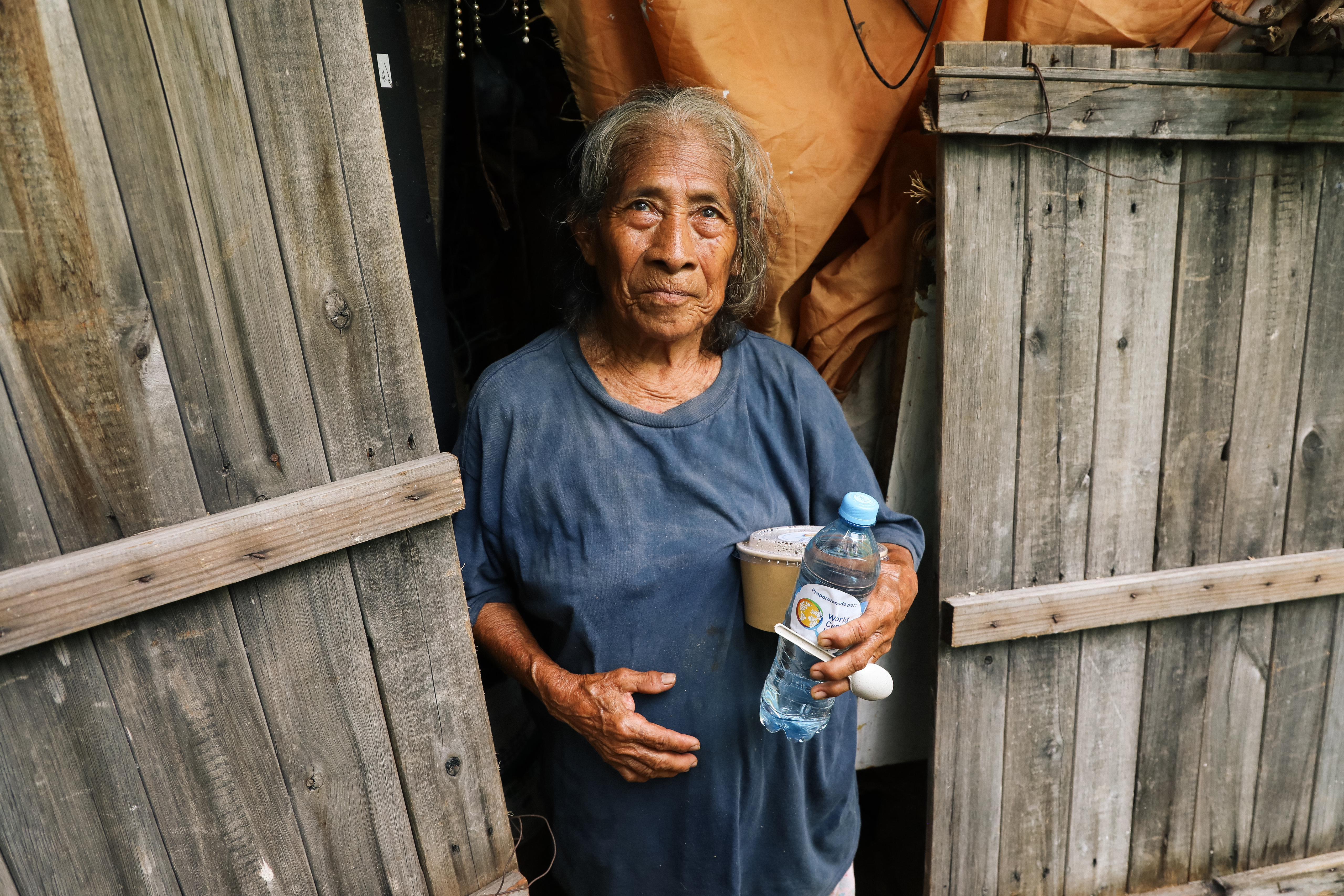 Margarita stands in front of her home holding a WCK-provided meal.